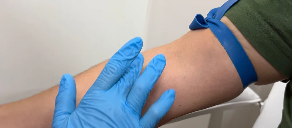 Una mà amb guant blau prepara el braç per a una extracció a Rápido Lab.