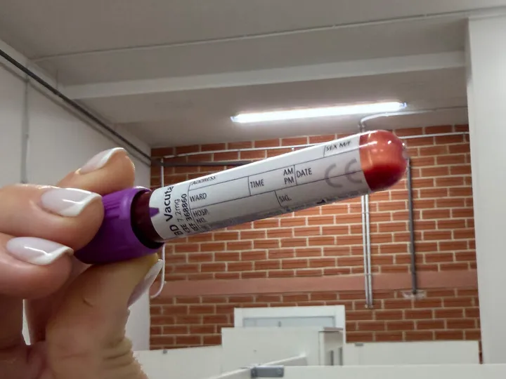 A hand holding a violet-capped tube with blank identification fields.