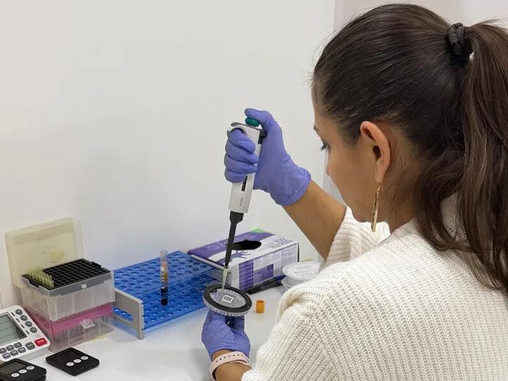 A laboratory professional using a micropipette and test disc.