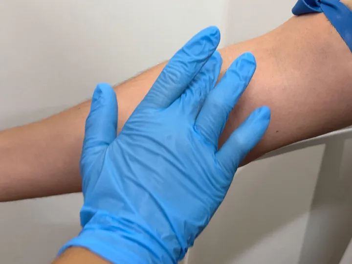 A blue-gloved hand preparing an arm for blood collection.