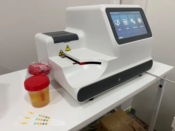 Urine test · 14 parameters. Urine analyser beside a sample container and reagent strips.